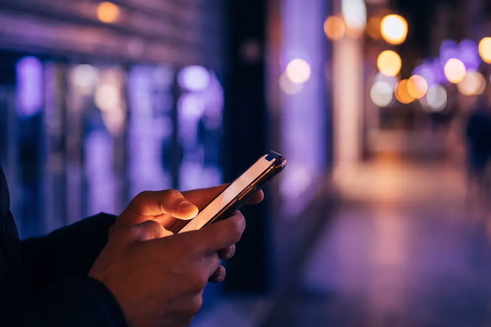 Unas manos escribiendo en el móvil en una calle comercial, de noche