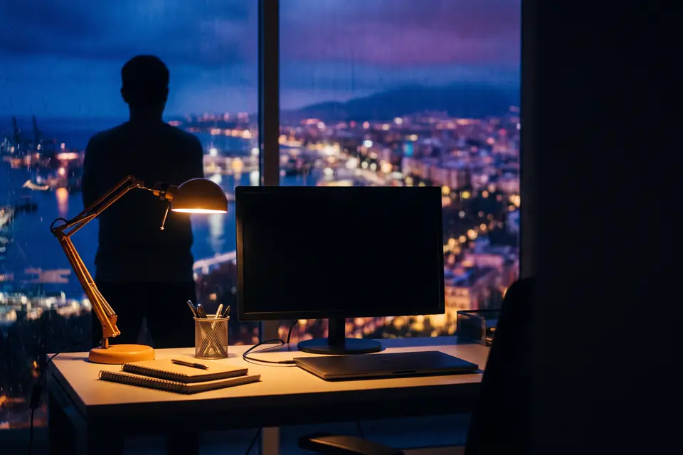 Una persona trabajando de noche en un despacho, con la ciudad iluminada al fondo