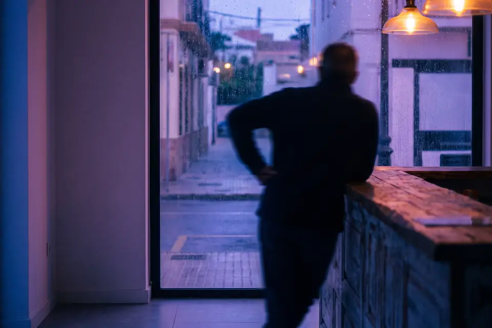 El dueño de un local apoyado en la barra, mirando a la calle al anochecer