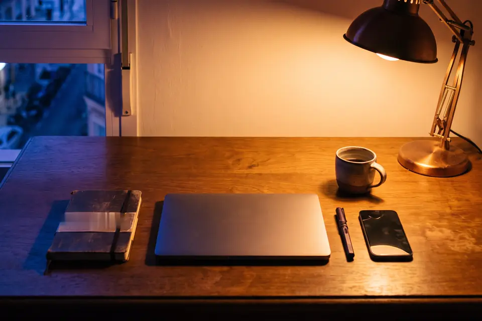 Un escritorio con libreta, portátil y café al caer la tarde