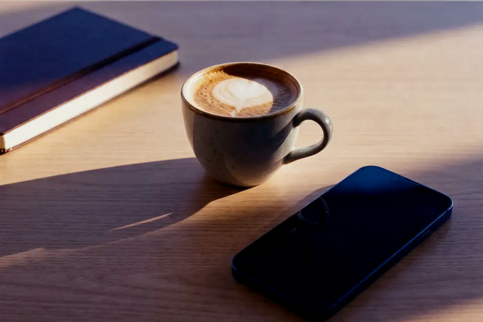 Una libreta, un café y un móvil sobre una mesa a primera hora
